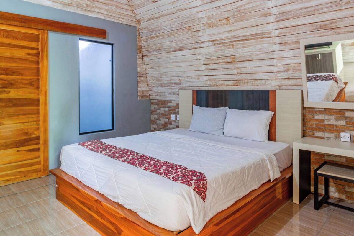 Une chambre avec un lit en bois, une petite table de chevet, un miroir et un mur décoré d’un motif en briques.