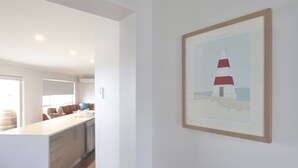A modern kitchen with a white countertop and cabinets, a dining area with a brown sofa, and a framed picture of a lighthouse on the wall. - Guichen Villa 3 - Wi-Fi, Pets welcome outside (Robe)