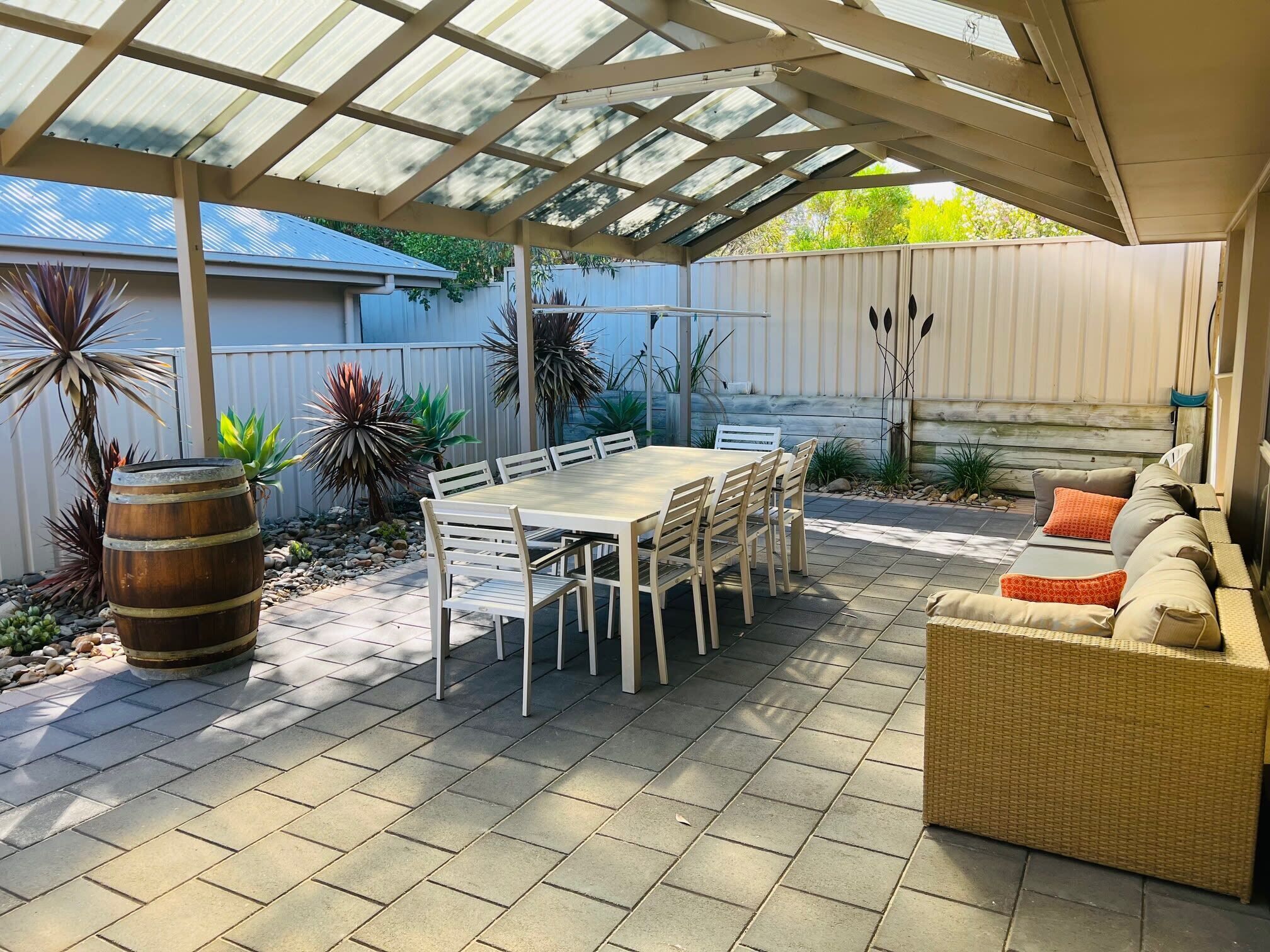 Patio esterno con zona salotto coperta, tavolo e diverse piante.
