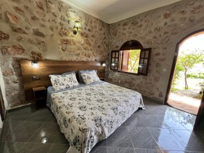 A bedroom with a stone wall, a wooden headboard, a bed with floral bedding, a nightstand, and a window with shutters.