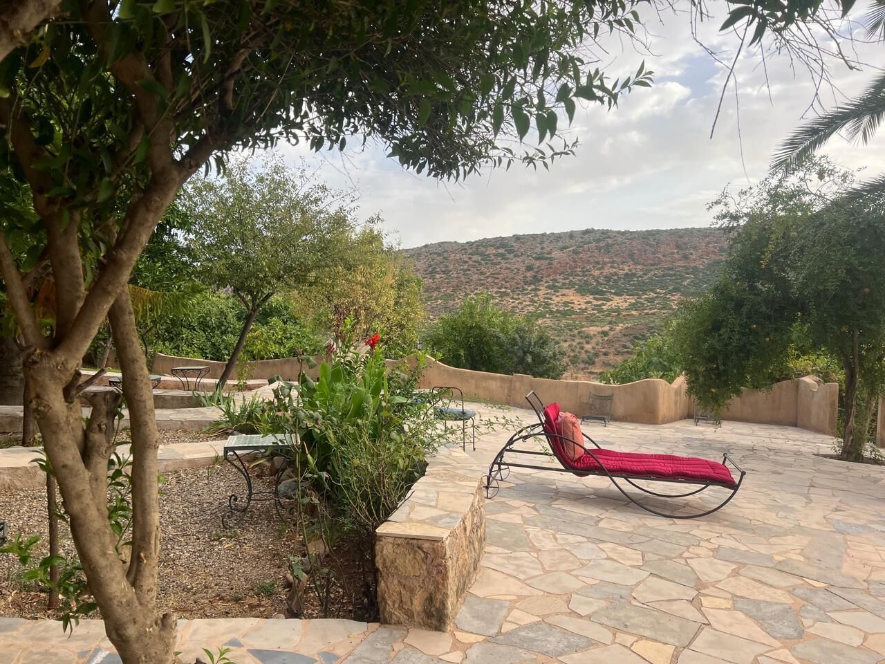 A patio with a lounge chair, stone flooring, and a view of a hilly landscape.