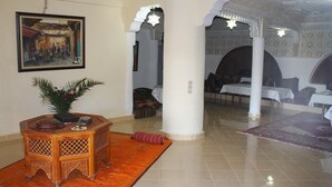 A lobby with a wooden side table, a potted plant, and a painting on the wall. - Azzaouia Resort & development (Bouchfaa)
