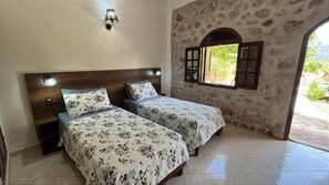 A bedroom with two beds, a wooden headboard, a wall-mounted light, and a window with shutters.