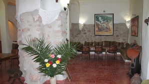 A dining area with a rustic stone pillar, a table with chairs, and a wall-mounted painting. - Azzaouia Resort & development (Bouchfaa)