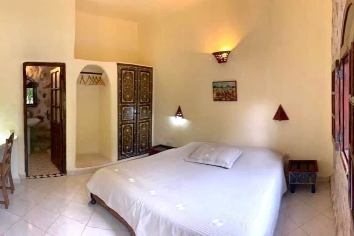 Une chambre à coucher comprenant un lit, un bureau, une chaise, une armoire et une petite table.