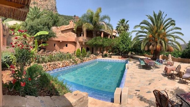 A pool area with a tiled deck, lounge chairs, and a palm tree. - Azzaouia Resort & development (Bouchfaa)