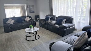 Uma sala de estar moderna com dois sofás de couro preto, uma mesa de centro redonda e uma janela grande com cortinas leves.