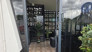 Entrada com porta de vidro, um pátio ladrilhado, um vaso de planta e área de estar externa com mobiliário preto.