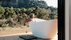 A person relaxing in a large bathtub with a view of a forested hillside. - Tiny Aura. (Coxs Crown)