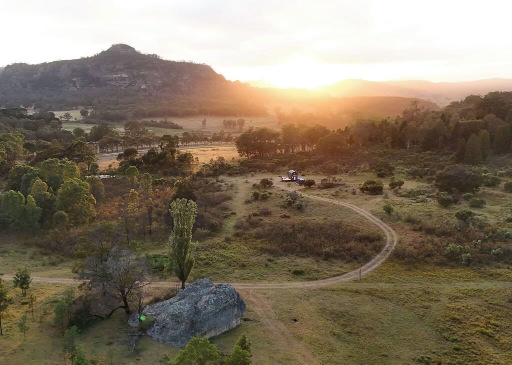 Ländliche Landschaft mit einer kurvenreichen Straße, einem kleinen Gebäude und einem großen Felsen im Vordergrund.