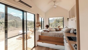 A modern bedroom with a large window, a ceiling fan, and a view of the outdoors. - Tiny Aura. (Coxs Crown)