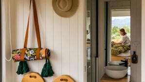 Un baño con un ventanal grande, un tocador de madera, un lavabo blanco y un sombrero colgado.