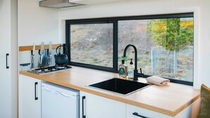 A modern kitchen with a wooden countertop, a black sink, and a window providing a view of greenery outside. - Tiny Matilda Summary: (Bridgetown)