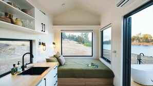 A compact room with a large window, a built-in bench, a sink, and a bathtub. - Tiny Matilda Summary: (Bridgetown)