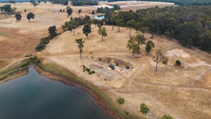 An aerial view of a rural landscape with a lake, scattered trees, and a dirt road. - Tiny Matilda Summary: (Bridgetown)