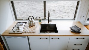 A compact kitchen with a gas stove, kettle, sink, and a view of the beach through a large window. - Tiny Pip Summary:<br>Tin (Tooborac)