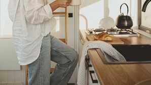 A person standing by a wooden ladder in a kitchen with a window, a kettle, and a cutting board with a croissant. - Tiny Rosie Summary:<br>S (Mount Crawford)