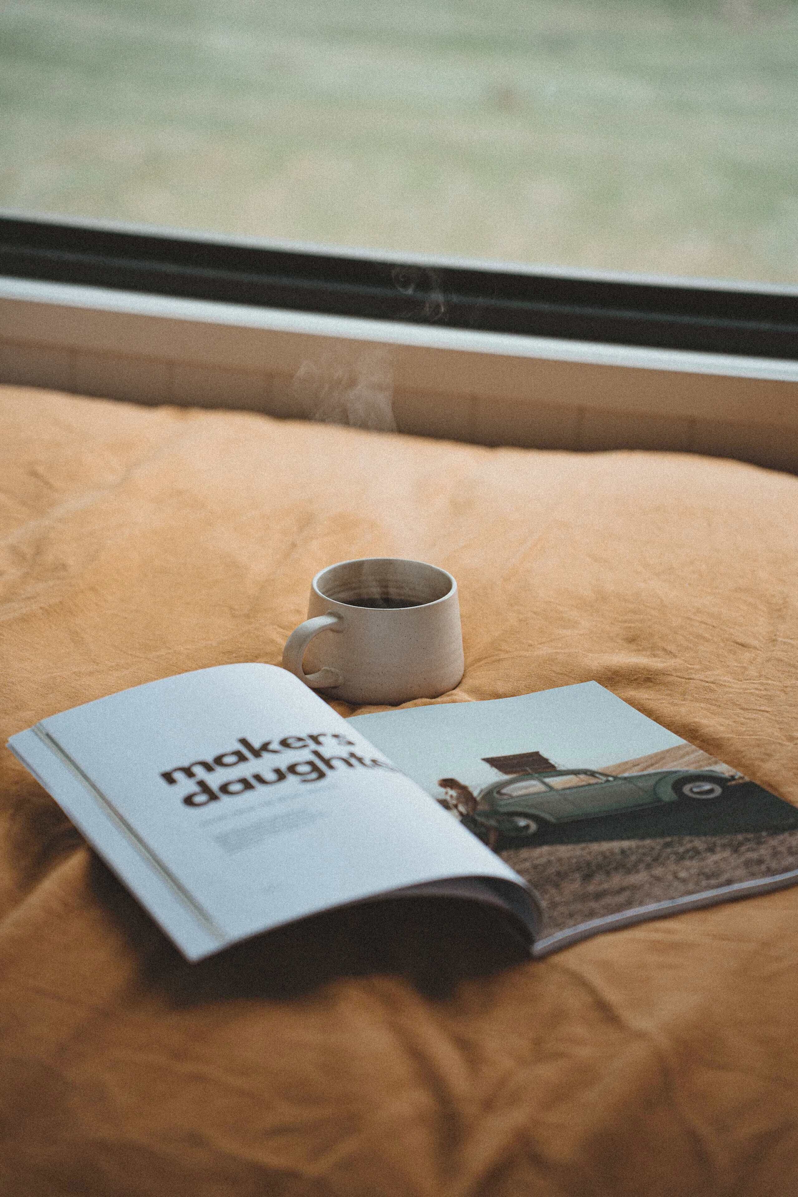 A magazine on a bed with a cup.