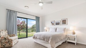 Un dormitorio con una cama, dos mesitas de noche con lámparas, una silla y un ventanal con cortinas.