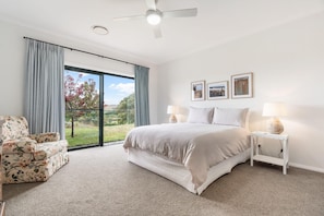 A bedroom with a bed, two bedside tables with lamps, a chair, and a large window with curtains.