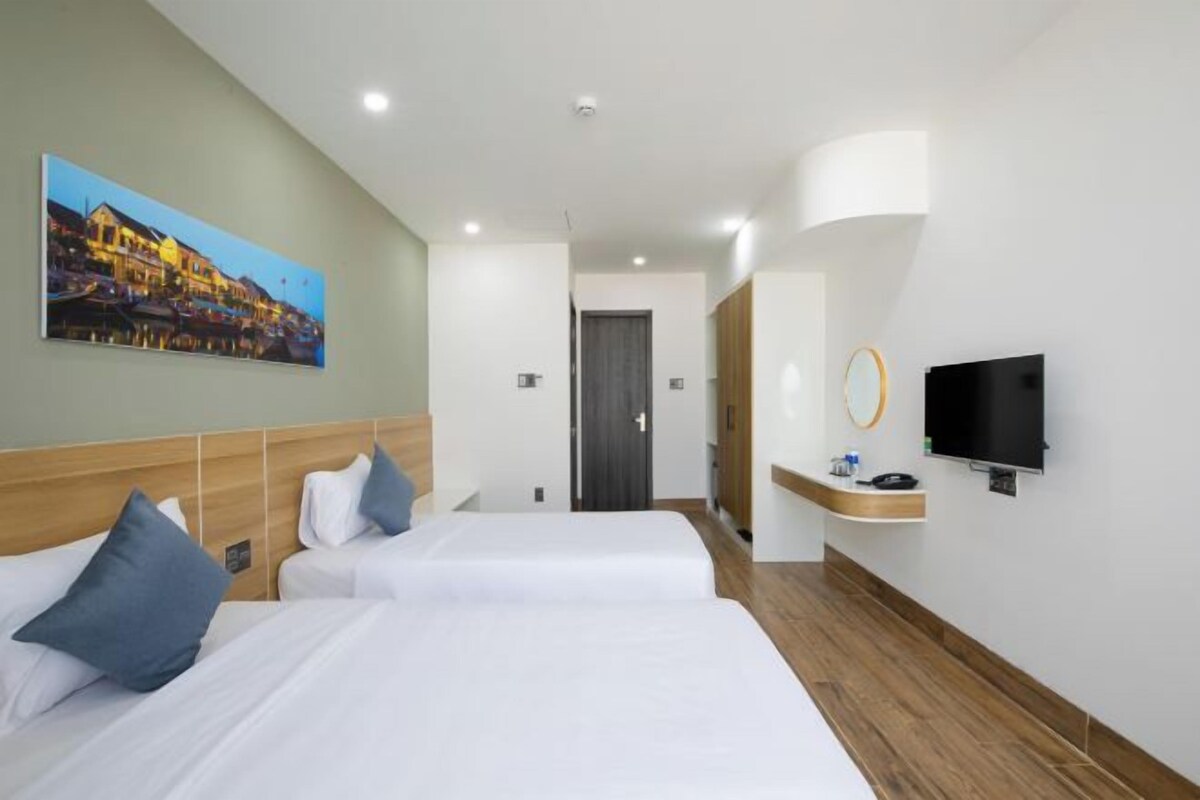 Quarto de hotel com duas camas, uma televisão, um quadro e piso de madeira.