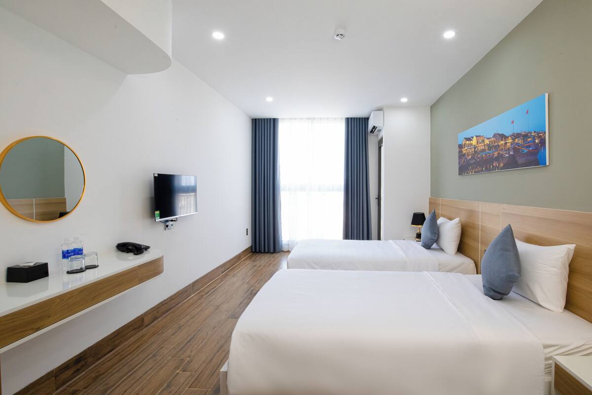 A hotel room with two beds, a TV, a mirror, a wooden floor, and a painting on the wall.