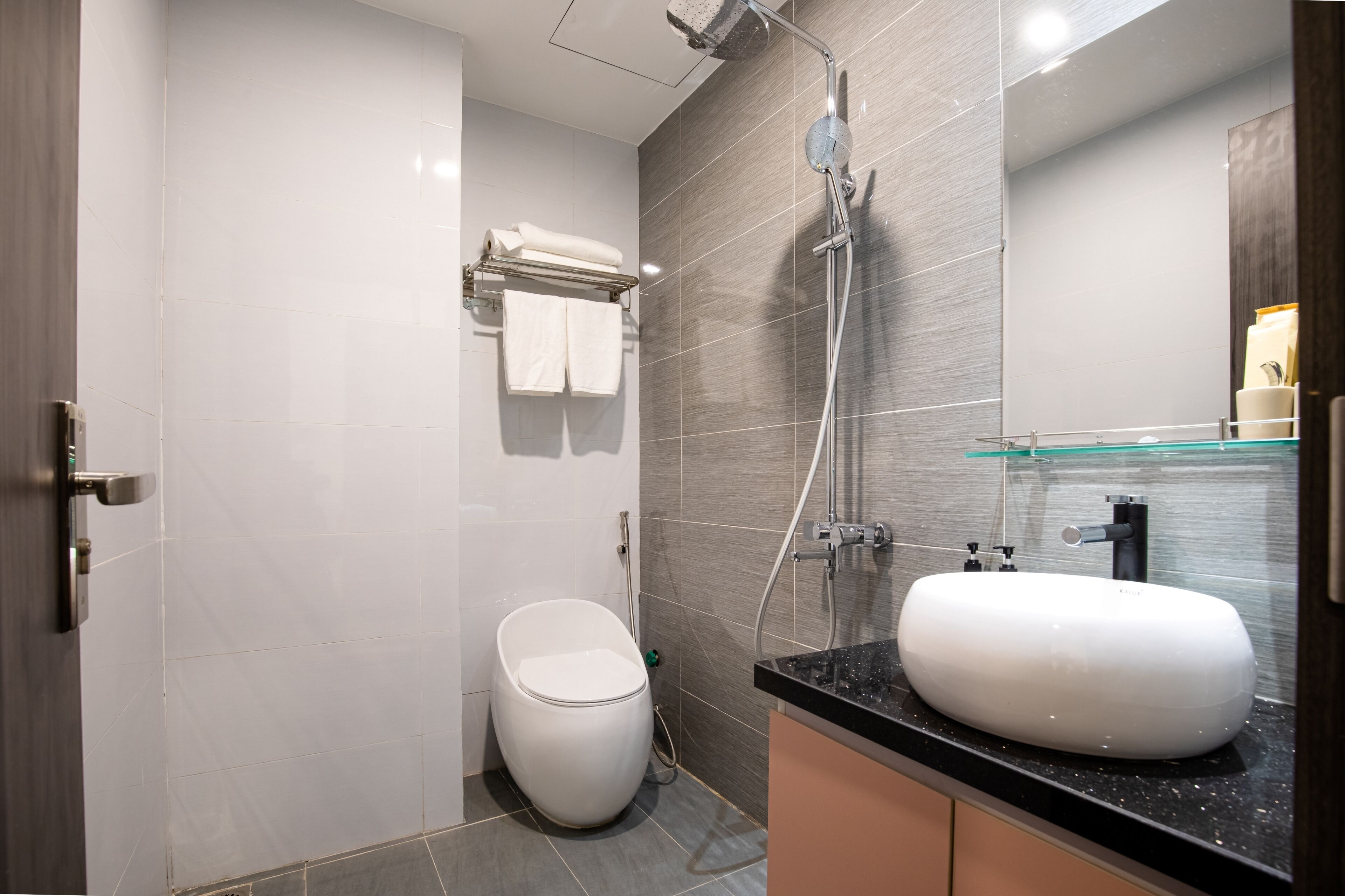 A modern bathroom with a white toilet, a glass shower enclosure, and a black countertop with a white sink.