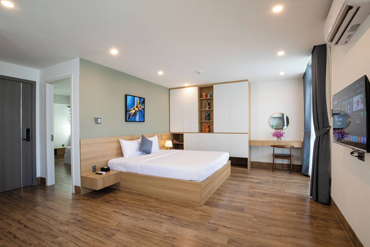 A modern hotel room with a wooden bed, a desk with a chair, a TV, and a wardrobe.