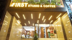 A building with a sign reading "FIRST STUDIO & COFFEE" at the entrance, featuring a staircase, potted plants, and a reception area. - FIRST Studio Hotel Da Nang (Da Nang)
