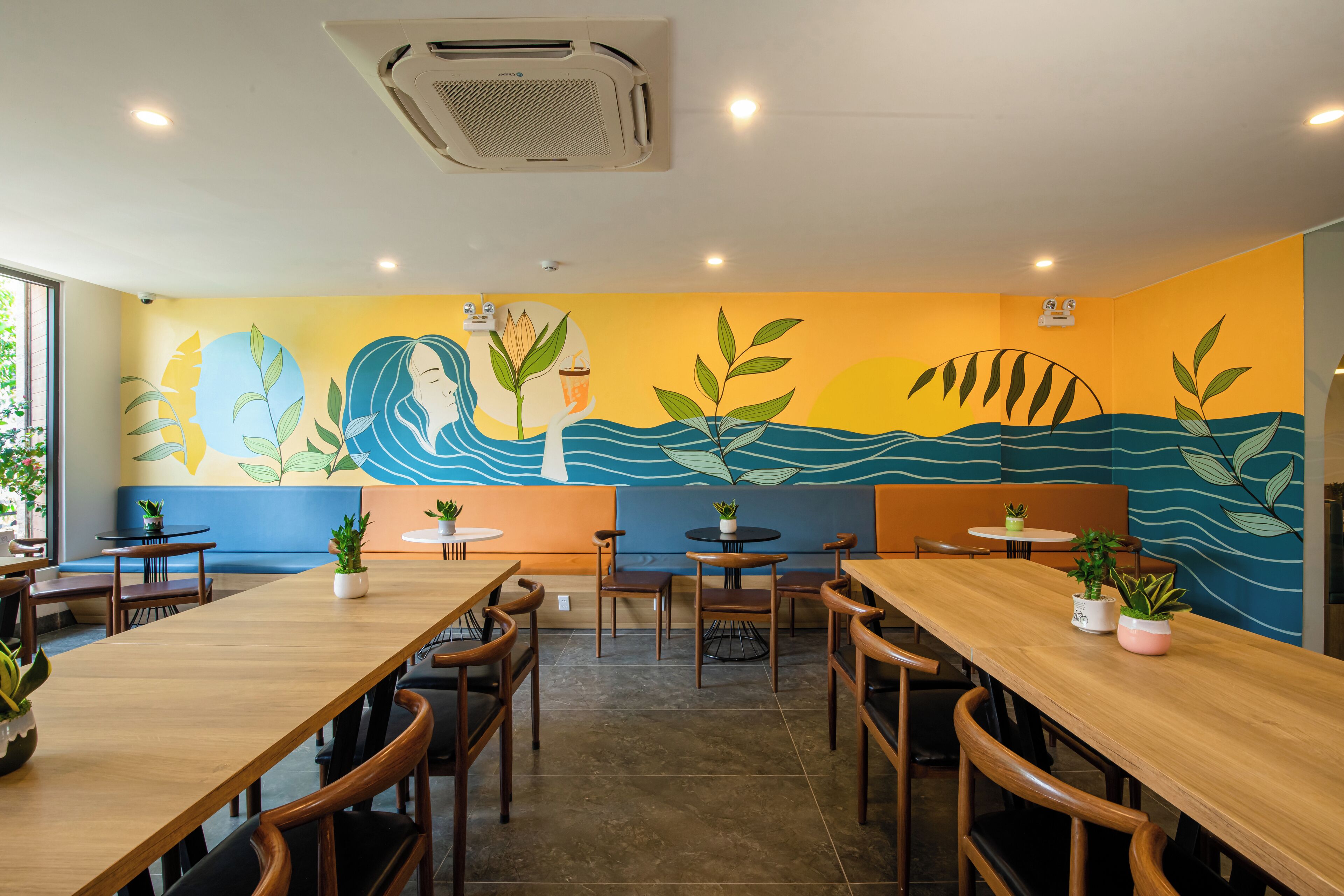 Restaurante com mesas e cadeiras de madeira, plantas em vasos e um mural com padrão de onda.