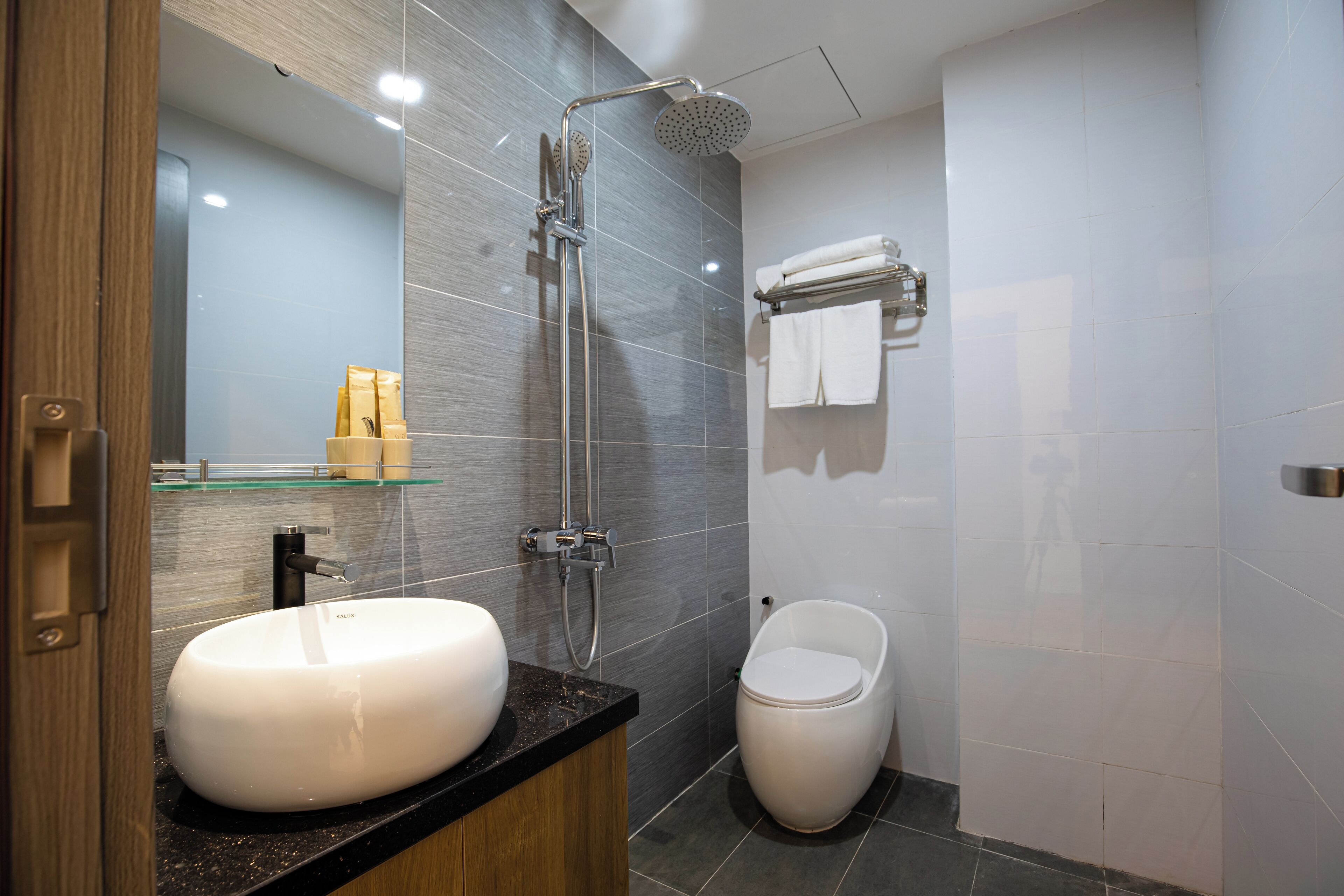 Un baño moderno con un lavamanos grande de color blanco, un estante de vidrio, una ducha con cabezal de ducha de mano y un inodoro.