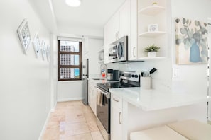 A compact kitchen with white cabinets, a microwave, stove, and a sink.