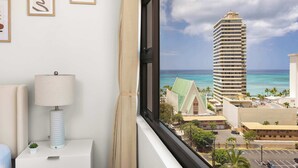 A hotel room with a view of a tall building, a lamp, and framed artwork on the wall. - Waikiki Banyan condo w/ ocean & skyline views (Honolulu)
