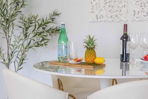 A round glass table with a bottle of water, a pineapple, and a bottle of wine.