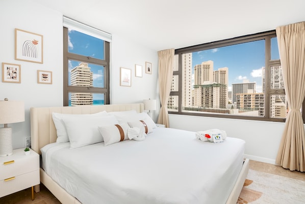 A hotel room with a bed, a nightstand, a lamp, a window with curtains, and framed pictures on the wall.