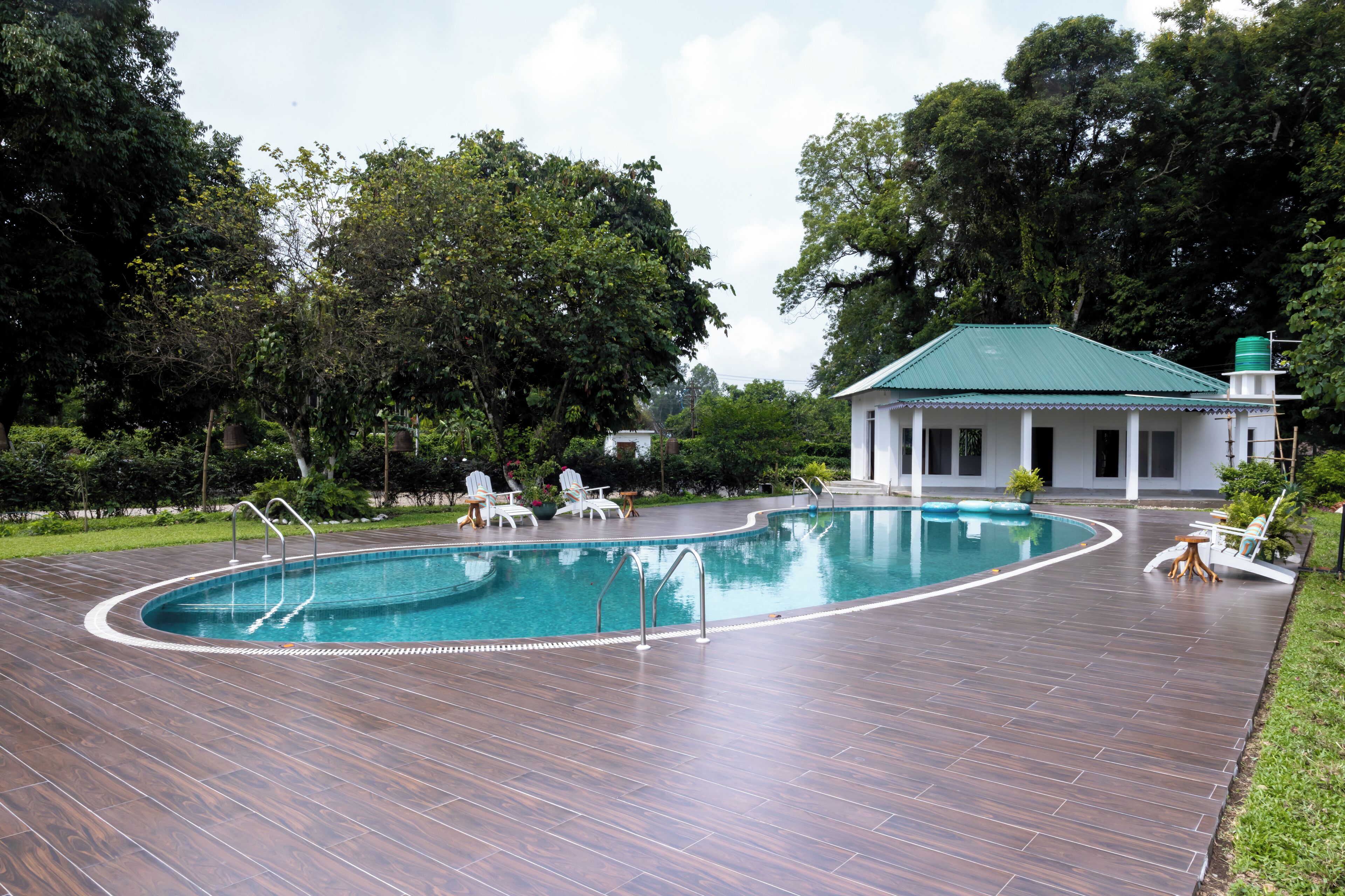 A swimming pool with a curved edge, surrounded by a wooden deck. There are lounge chairs and a small table near the pool.