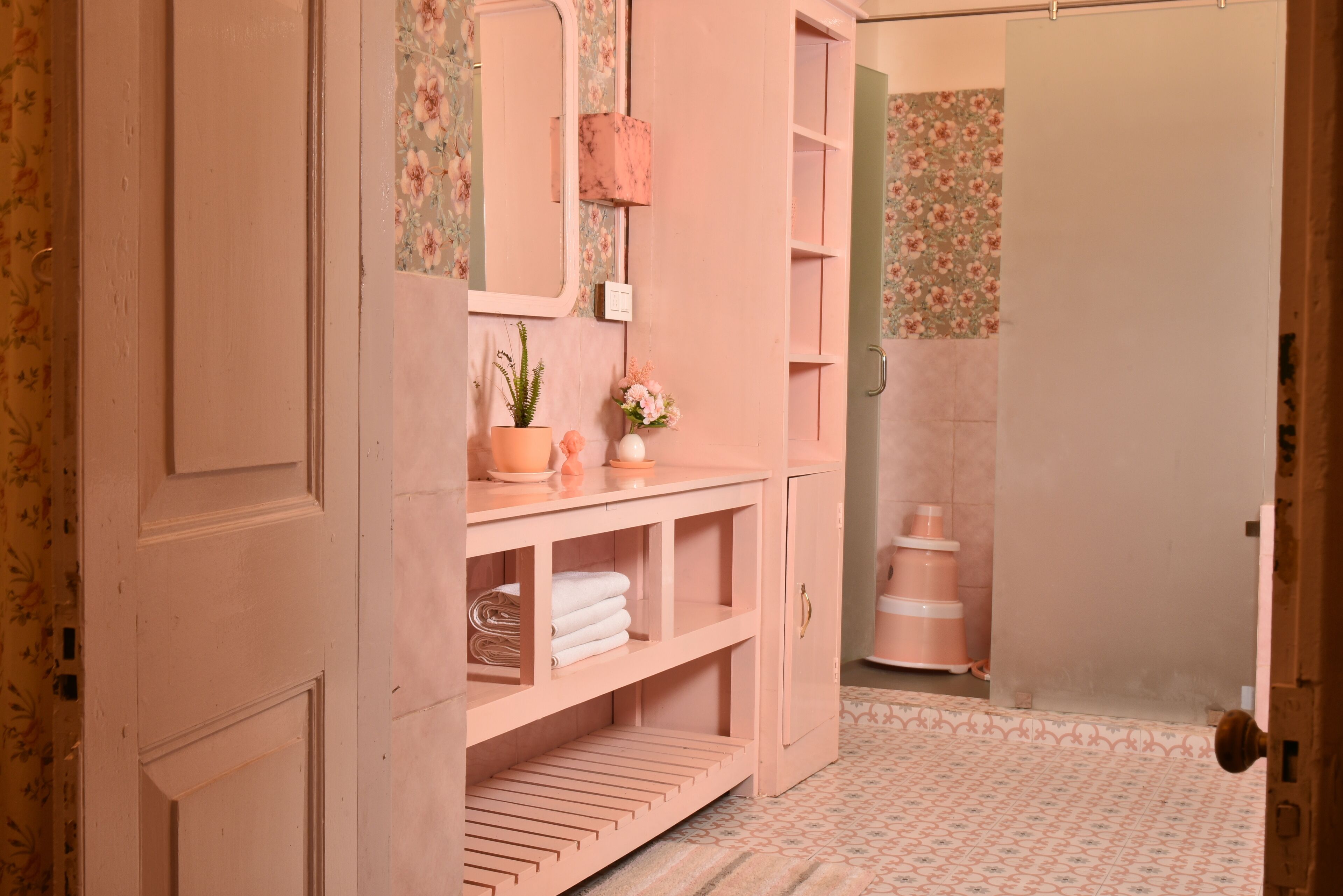 A pink bathroom with a vanity, shelves, and a mirror.