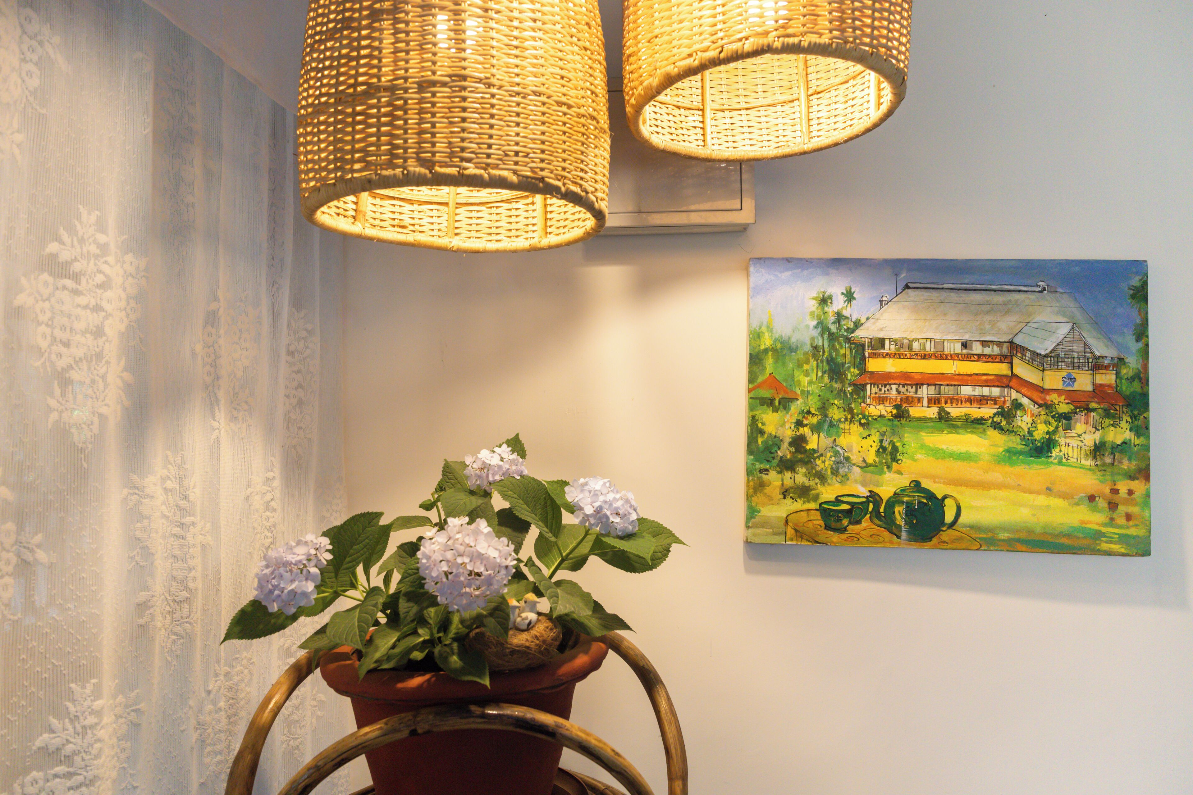 Una habitación con una planta en maceta, lámparas de mimbre y un cuadro de una casa.