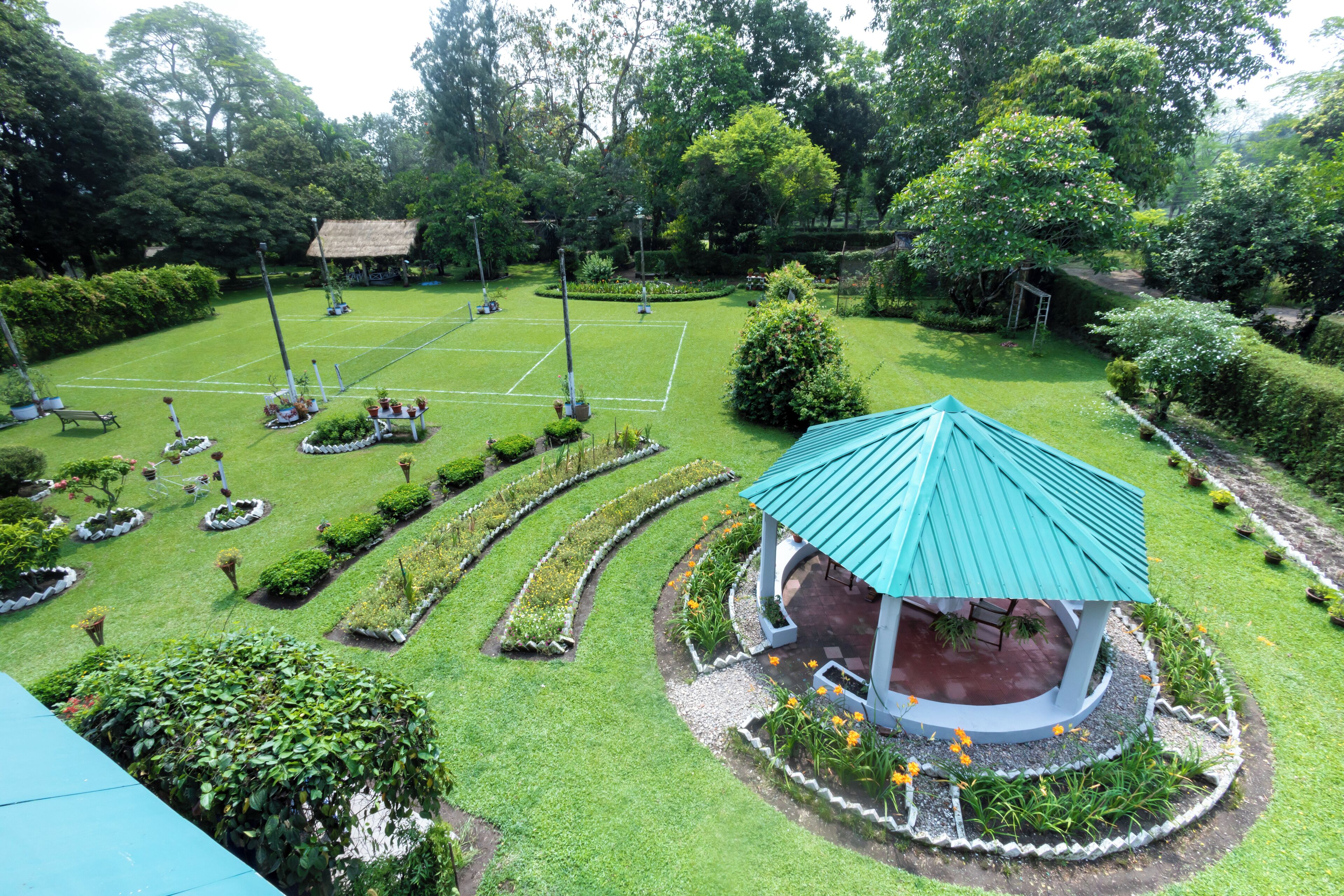 Un jardín bien cuidado con un pabellón, setos recortados y una cancha de tenis.