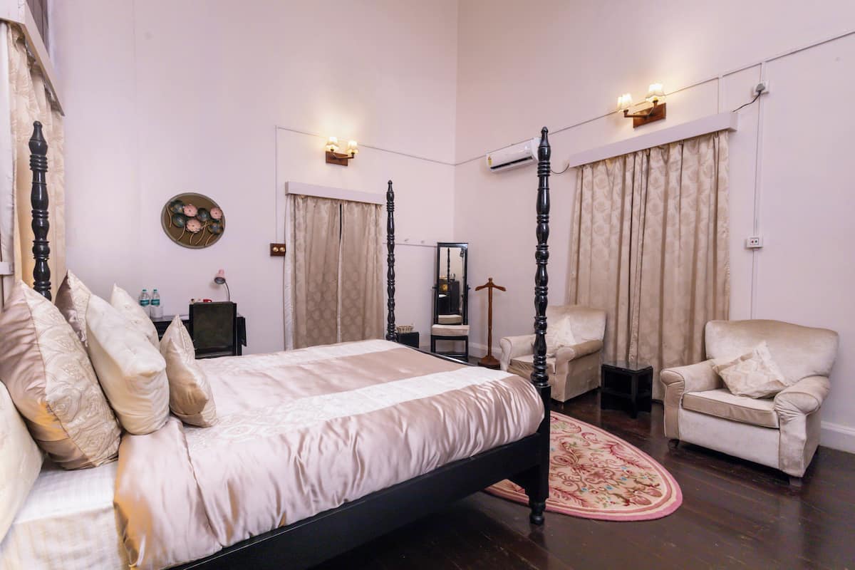 Ein Schlafzimmer mit einem Himmelbett, einem Sessel, einem kleinen Tisch und einem Spiegel.