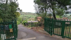 A gated entrance with a pathway leading to a building. - In the Green near the Sea (Orbetello)