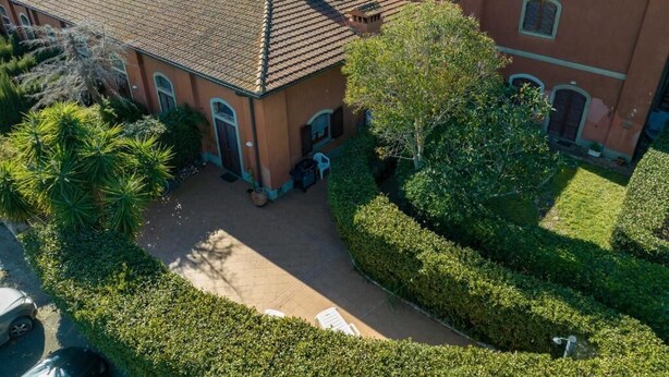 An aerial view of a building with a tiled roof, surrounded by well-maintained hedges and a few trees. - In the Green near the Sea (Orbetello)