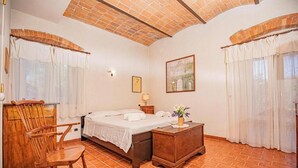 Une chambre à coucher avec un lit, une chaise en bois, une table de chevet et un tableau accroché au mur.