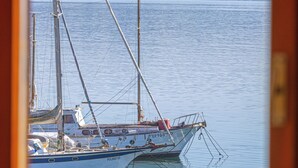 A view of a harbor with a sailboat docked, calm water, and a hilly landscape in the background. - View of the harbour (Orbetello)