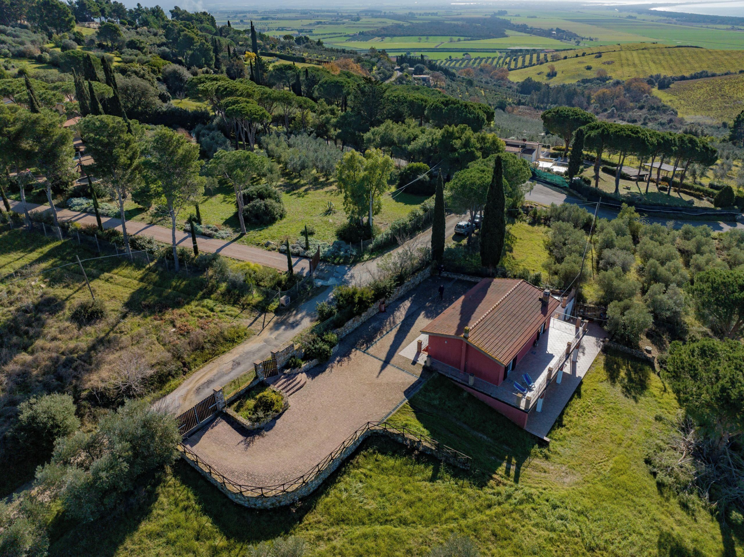 Una casa rural con techo rojo, rodeada de vegetación y campos.