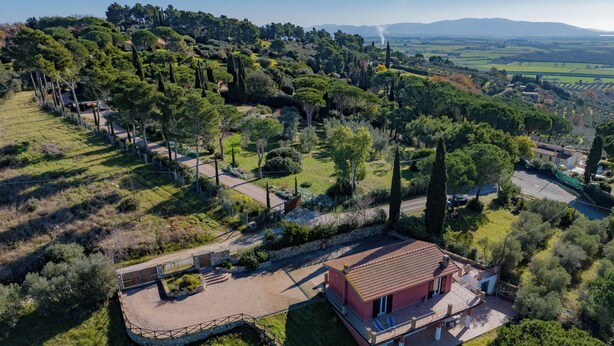 A red villa with a stone pathway leading to the entrance, surrounded by lush greenery and trees. - The View of Talamone (Orbetello)