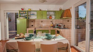 A dining area with a table set for four, green cabinets, a tiled backsplash, and a sliding glass door leading to an outdoor patio. - The View of Talamone (Orbetello)