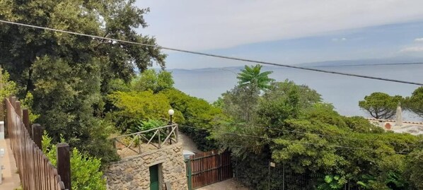 Vista de una zona costera con un edificio de piedra, una valla de madera y abundante vegetación.