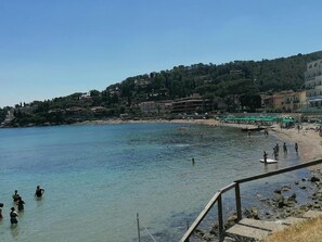 A coastal area with clear water, a sandy beach, and buildings on a hillside. - The Terrace on the Beach (Grosseto)