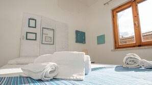 A hotel room with a bed, a window, and a wall with framed pictures. - The sea is close at hand. (Orbetello)